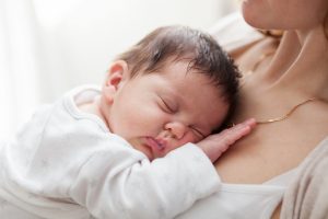 Young mother is holding her sleeping newborn baby